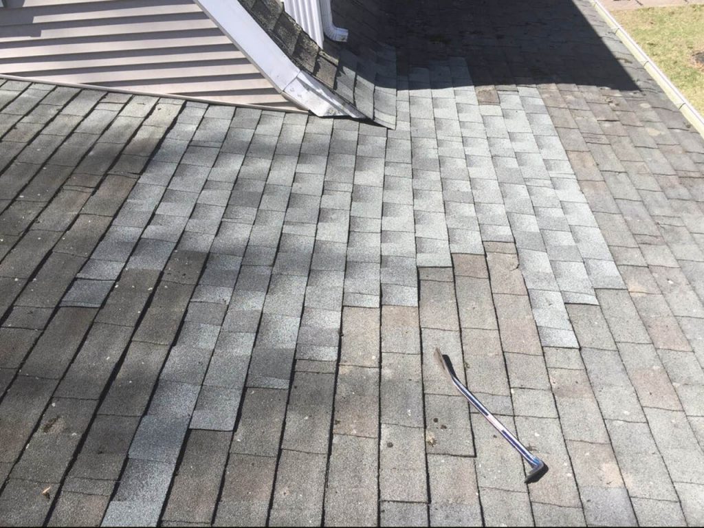 A close view of a shingle roof with visible lines and patterns in the roofing material, showing a repair zone where shingles appear adjusted or disturbed as part of an ongoing effort to address water intrusion or roof surface issues.