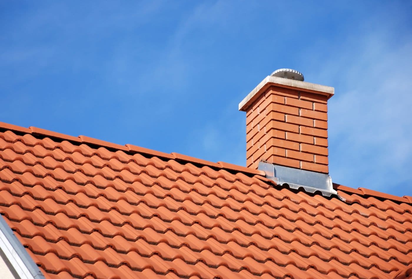 Chimney and roof with red clay tiles and brick chimney on a residential home in Long Island, NY.
