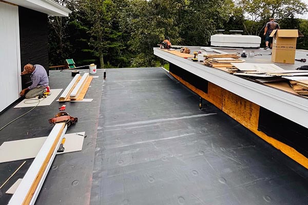 Roof installation on a residential building in Long Island, NY, with workers actively working on the flat roof surface.