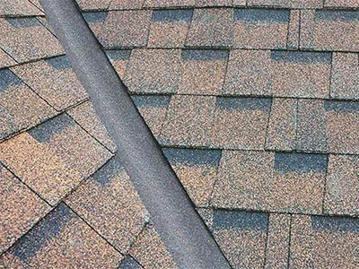 Close-up view of an asphalt shingle roof with a ridge, installed by a professional roofer Long Island. Overlapping brown and gray rectangular shingles are arranged in neat rows, highlighting expert craftsmanship.