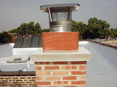 A brick chimney with a red clay flue and metal cap sits on a flat, white rooftop. Trees and buildings are visible under a clear NY sky—perfect inspiration for any roofer Long Island trusts.