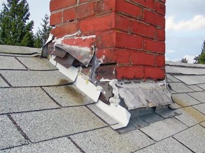 Damaged chimney flashing and brick chimney on roof with deteriorated shingles, requiring professional repair to prevent leaks and water damage.